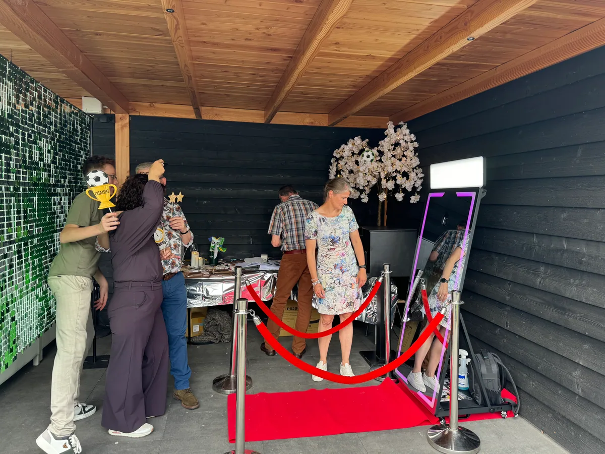Gasten gebruiken feestprops naast de Mirror Booth met rode loper en afzetpalen.
